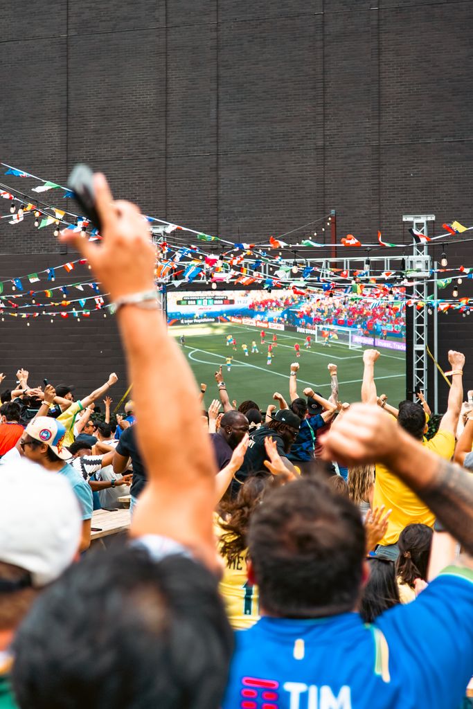 A vibrant crowd cheerfully watching a soccer match on a big screen in Chicago, adorned with colorful flags.